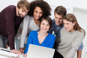 Team leadership and success with a pretty young businesswoman sitting at a laptop computer surrounded by a group of motivated young team members