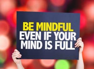 image of person holding sign that reads BE MINDFUL EVEN IF YOU MIND IS FULL