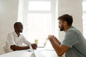 African-american and caucasian businessmen talking laughing having fun at workplace, diverse colleagues joking sharing ideas at office desk, good relations in team and multiracial friendship at work