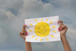 person holding up piece of paper with sun smiley face on it