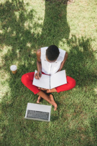 Woman sitting on grass with paper and computer working