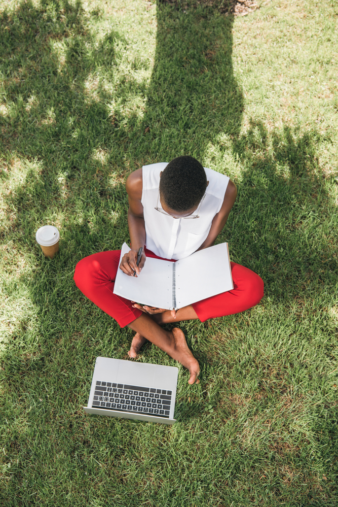 Woman sitting on grass with paper and computer working