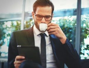 Man drinking coffee in a suit while checking is tablet for email