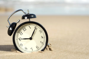 Black alarm clock sitting on a beach inspiring you to take time for self-care